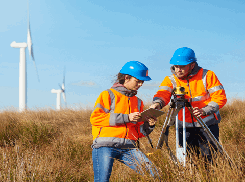 Two people wearing orange high vis jackets looking at a clipboard in a wind farm field