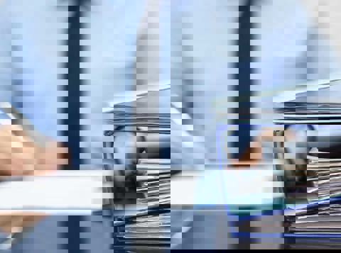 Man in business attire writing notes with a binder on the desk in front of him